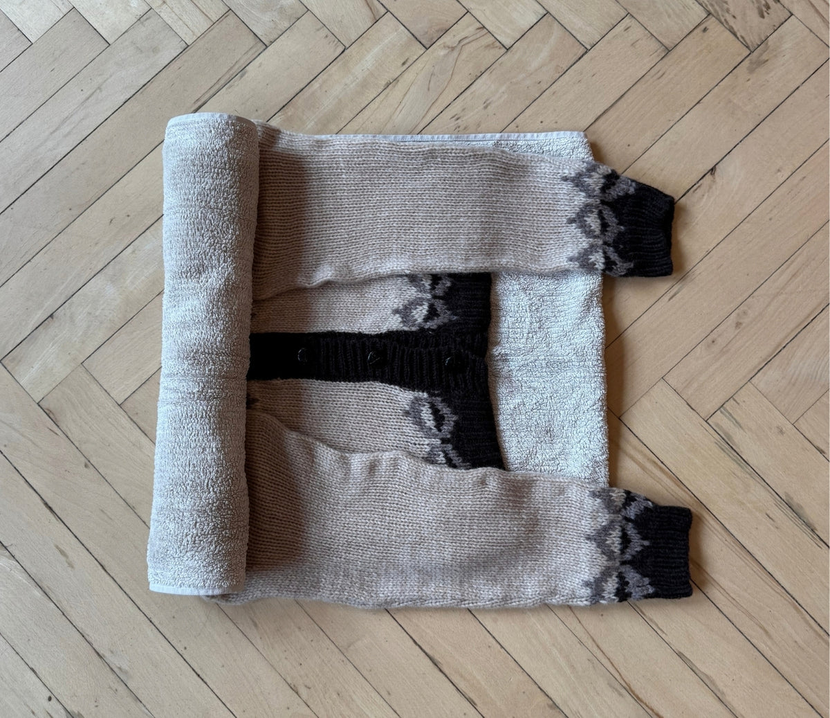 Bild eines Strickpullovers, der auf einem Handtuch liegt. Das Handtuch wird zusammengerollt, damit es einen Teil des überschüssigen Wassers aus dem Pullover aufnimmt.