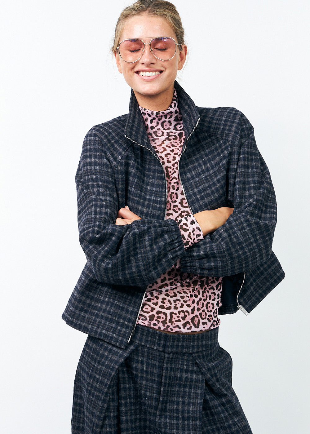 Model trägt ein kariertes Outfit in Blau – eine Wolljacke im Bomberstil und eine Hose mit Falten, darunter ein Rollkragenpullover im pinken Leopardenmuster.