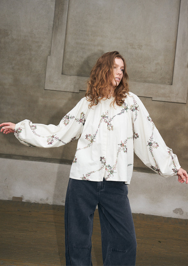Frau trägt eine cremefarbene Bluse mit gestickten Blumenmotiven und eine dunkle Jeans von Lollys Laundry.