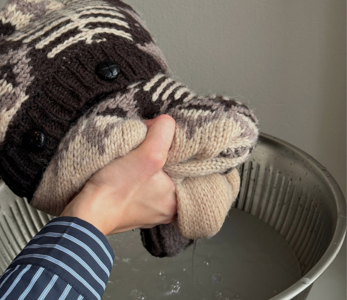 Bild eines Strickpullovers, der aus dem Wasser gehoben wird, während das überschüssige Wasser vorsichtig herausgedrückt wird.