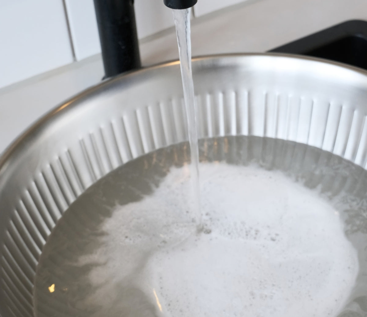 Bild von einem Waschbecken und einer Schüssel mit Wasser und Waschmittel, in der der Strickpullover gewaschen werden soll.