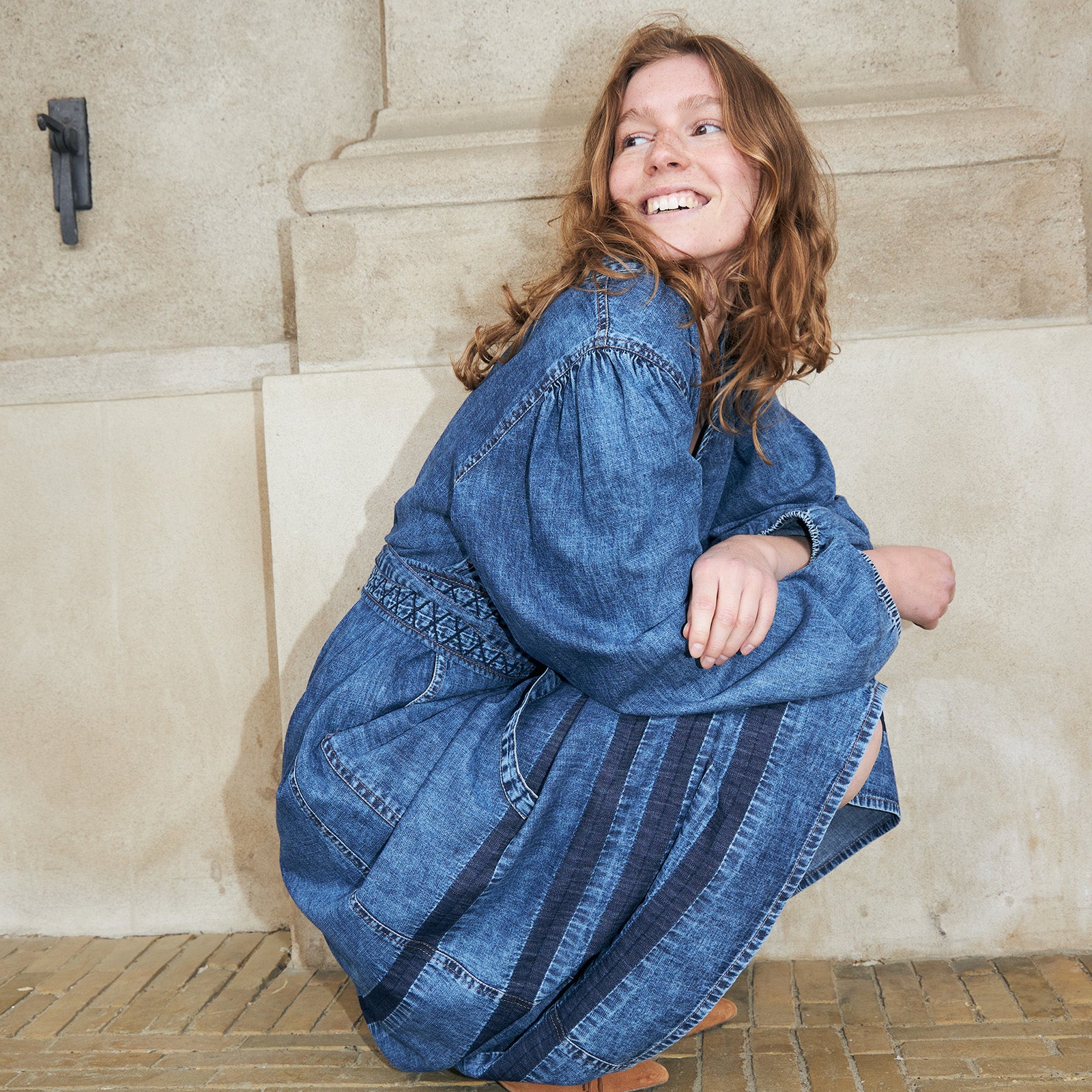 Frau trägt ein blaues Denimkleid mit bestickten Details und weiten Ärmeln. Ein lässiger und femininer Denim Look für den Alltag.