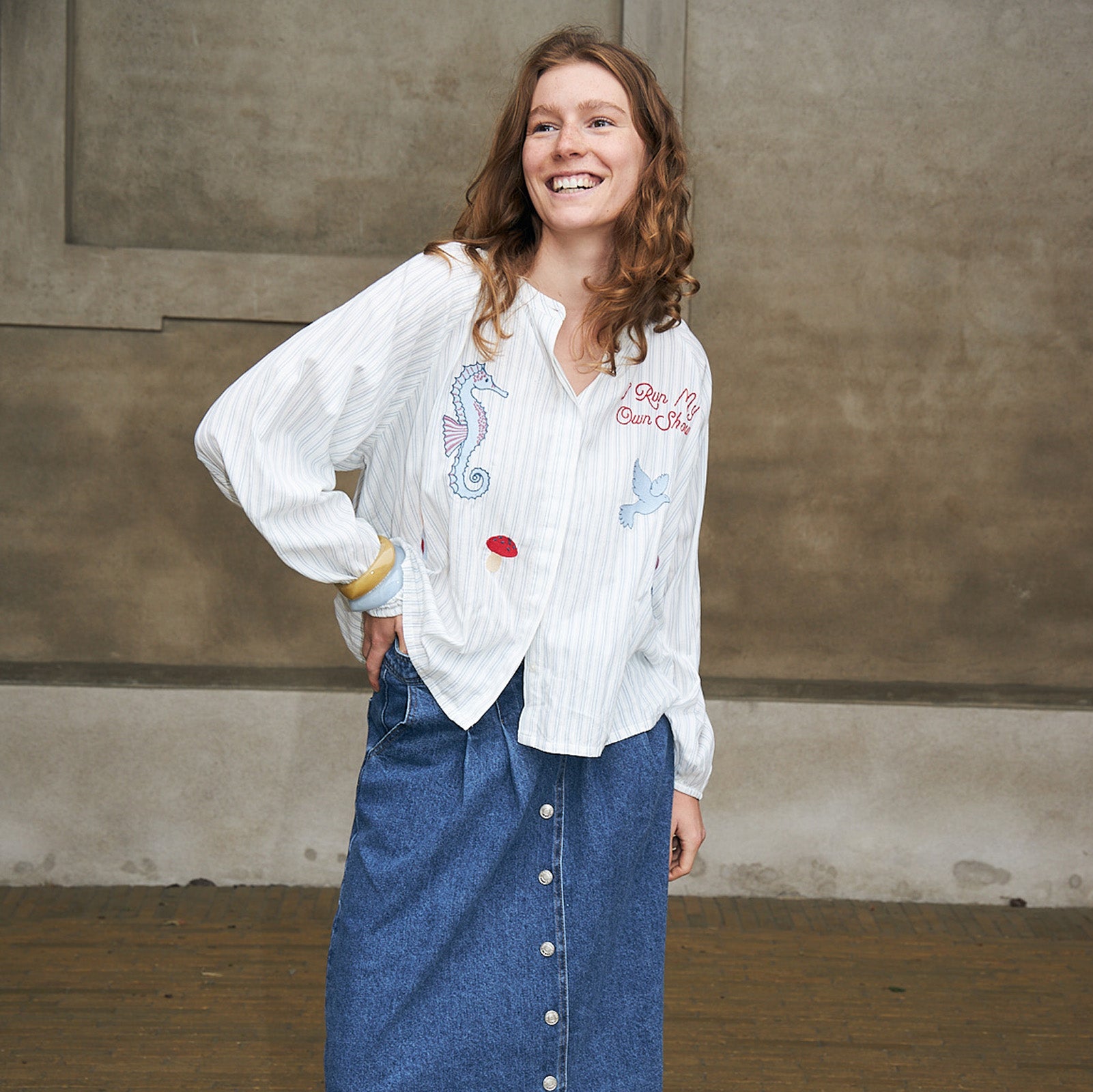 Frau trägt eine weiße bestickte Bluse mit farbenfrohen Motiven und einen blauen Jeansrock mit Knopfleiste vorne von Lollys Laundry.